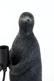 Nahaufnahme einer schwarzen Tischleuchte in Form eines Pinguins, der eine Lampenfassung hält.