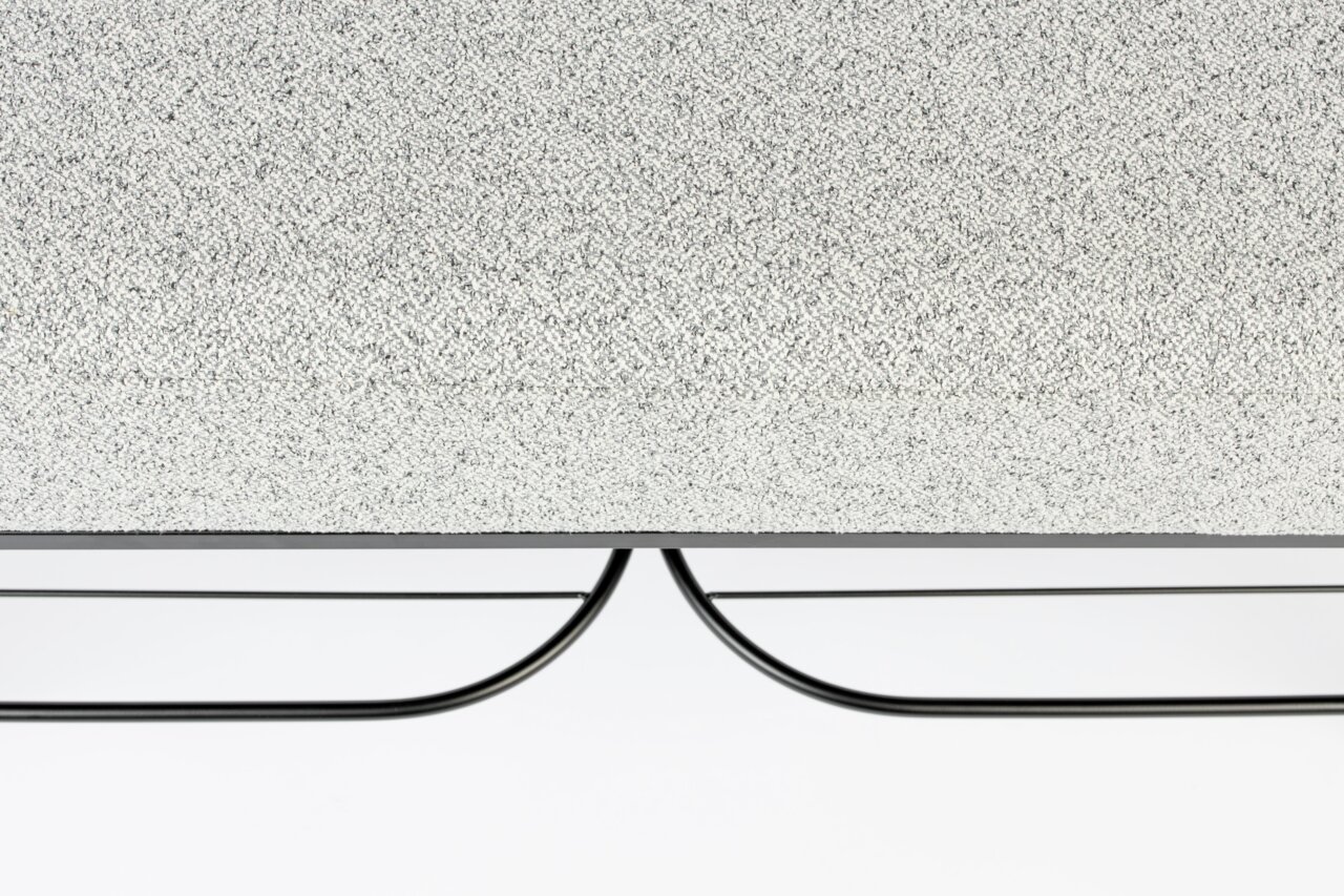 Nahaufnahme einer Sitzbank mit grauer, texturierter Oberfläche und schwarzem Metallgestell, von der Seite betrachtet.