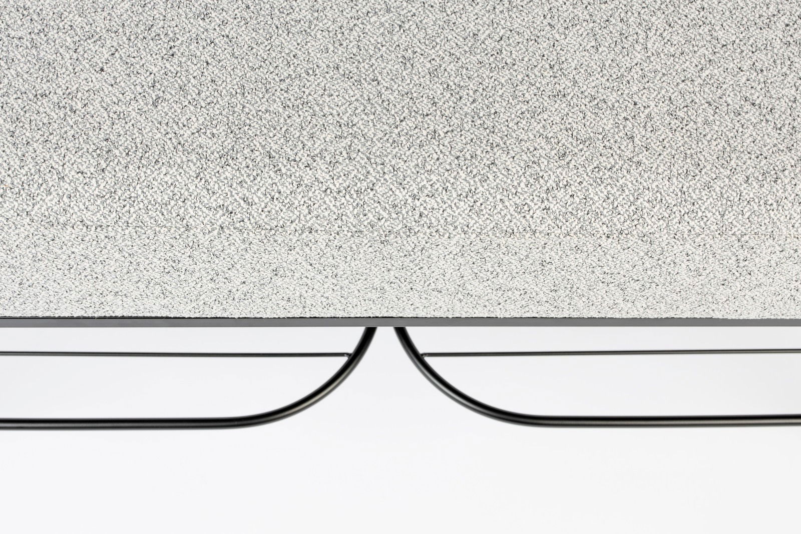 Nahaufnahme einer Sitzbank mit grauer, texturierter Oberfläche und schwarzem Metallgestell, von der Seite betrachtet.