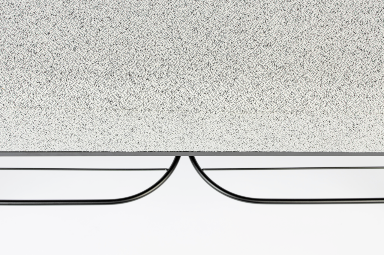 Nahaufnahme einer Sitzbank mit grauer, texturierter Oberfläche und schwarzem Metallgestell, von der Seite betrachtet.