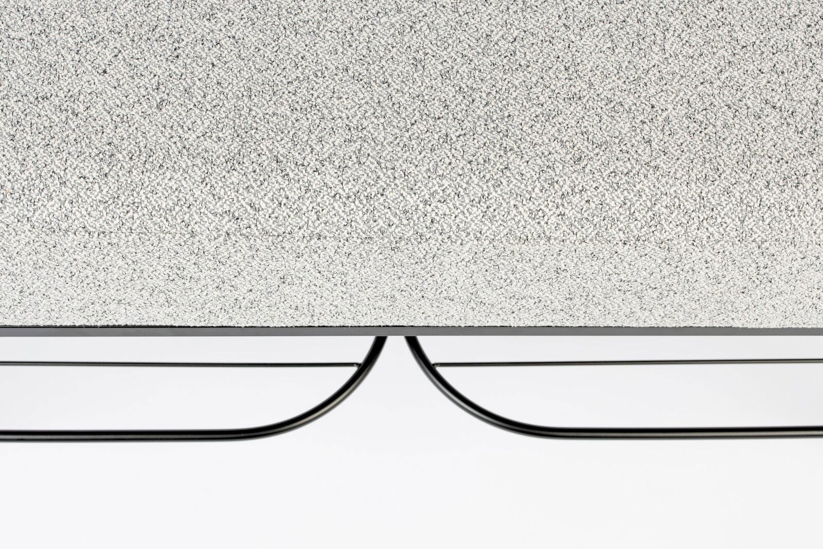 Nahaufnahme einer Sitzbank mit grauer, texturierter Oberfläche und schwarzem Metallgestell, von der Seite betrachtet.