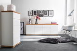 Moderne Wohnzimmermöbel mit weißem Hochkommode und Sideboard, Holzoberflächen, dekoriert mit Vasen und Blumen, seitliche Perspektive.