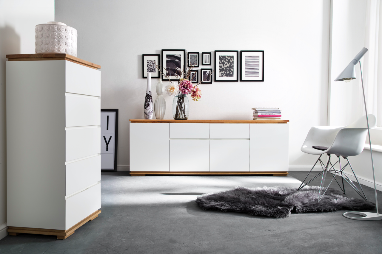 Zurbrüggen XL-Sideboard CHIARO Moderne Wohnzimmermöbel mit weißem Hochkommode und Sideboard, Holzoberflächen, dekoriert mit Vasen und Blumen, seitliche Perspektive.