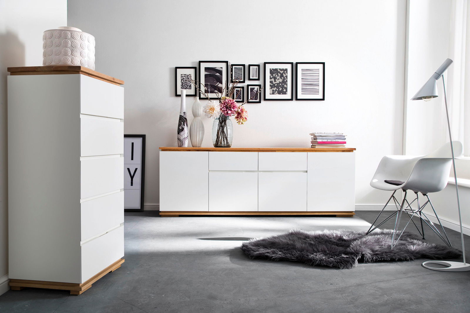 Moderne Wohnzimmermöbel mit weißem Hochkommode und Sideboard, Holzoberflächen, dekoriert mit Vasen und Blumen, seitliche Perspektive.