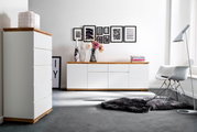 Moderne Wohnzimmermöbel mit weißem Hochkommode und Sideboard, Holzoberflächen, dekoriert mit Vasen und Blumen, seitliche Perspektive.
