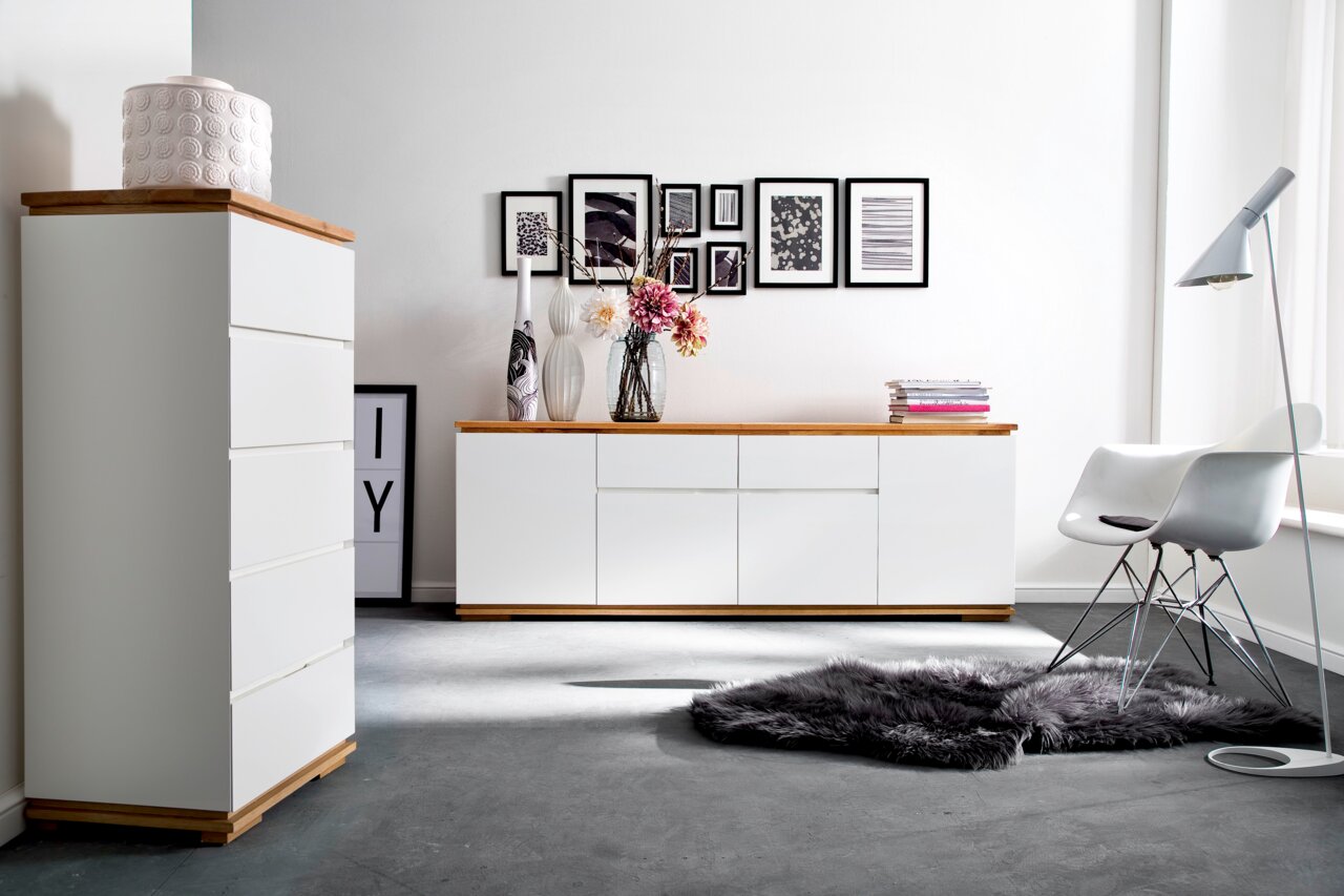 Moderne Wohnzimmermöbel mit weißem Hochkommode und Sideboard, Holzoberflächen, dekoriert mit Vasen und Blumen, seitliche Perspektive.
