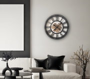 Moderne Wanduhr mit sichtbarem Zahnrad-Design, an einer Wohnzimmerwand über einem Sofa montiert, aus seitlicher Perspektive fotografiert.