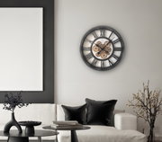 Moderne Wanduhr mit sichtbarem Zahnrad-Design, an einer Wohnzimmerwand über einem Sofa montiert, aus seitlicher Perspektive fotografiert.