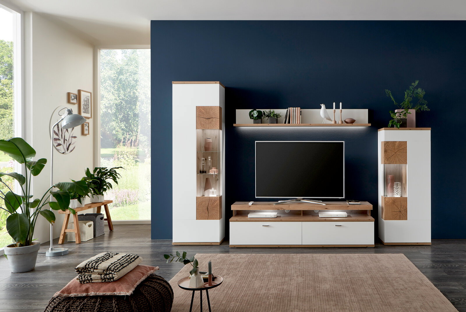 Moderne Wandkombination SYLT in einem Wohnzimmer mit dunkler Akzentwand, bestehend aus zwei hohen Schränken, einem TV-Board und einem Regal, frontal betrachtet.