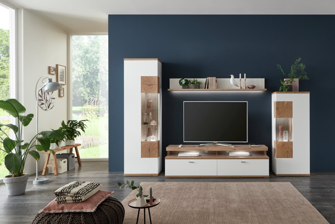Moderne Wandkombination SYLT in einem Wohnzimmer mit dunkler Akzentwand, bestehend aus zwei hohen Schränken, einem TV-Board und einem Regal, frontal betrachtet.