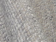 Nahaufnahme eines handgewebten Teppichs mit grauen und beigen Tönen, die Textur und Webart aus der Seitenperspektive zeigend.