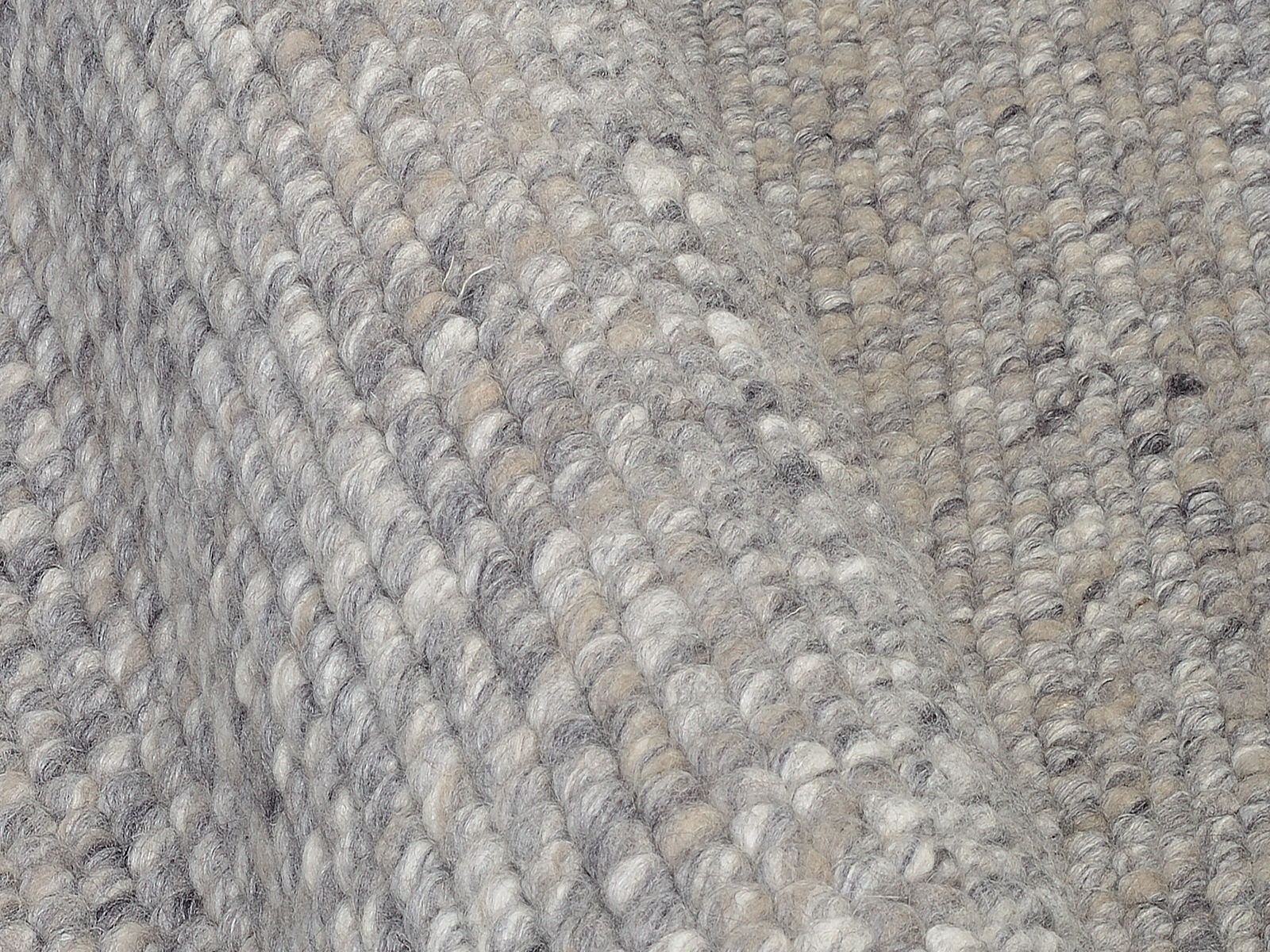 Nahaufnahme eines handgewebten Teppichs mit grauen und beigen Tönen, die Textur und Webart aus der Seitenperspektive zeigend.