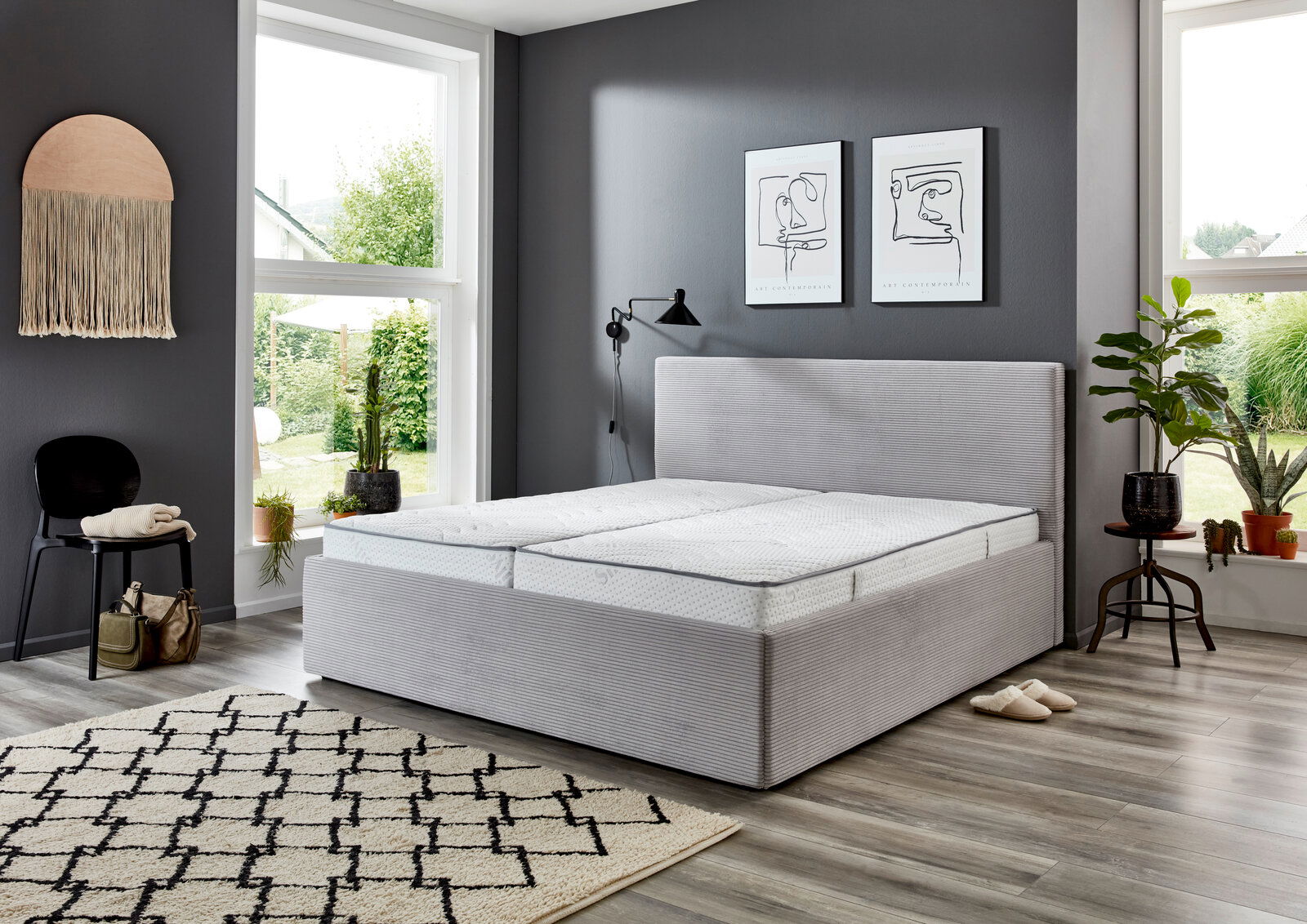 Modernes Polsterbett 160x200 in einem stilvollen Schlafzimmer mit grauer Wand, großen Fenstern und Pflanzen, seitliche Perspektive.