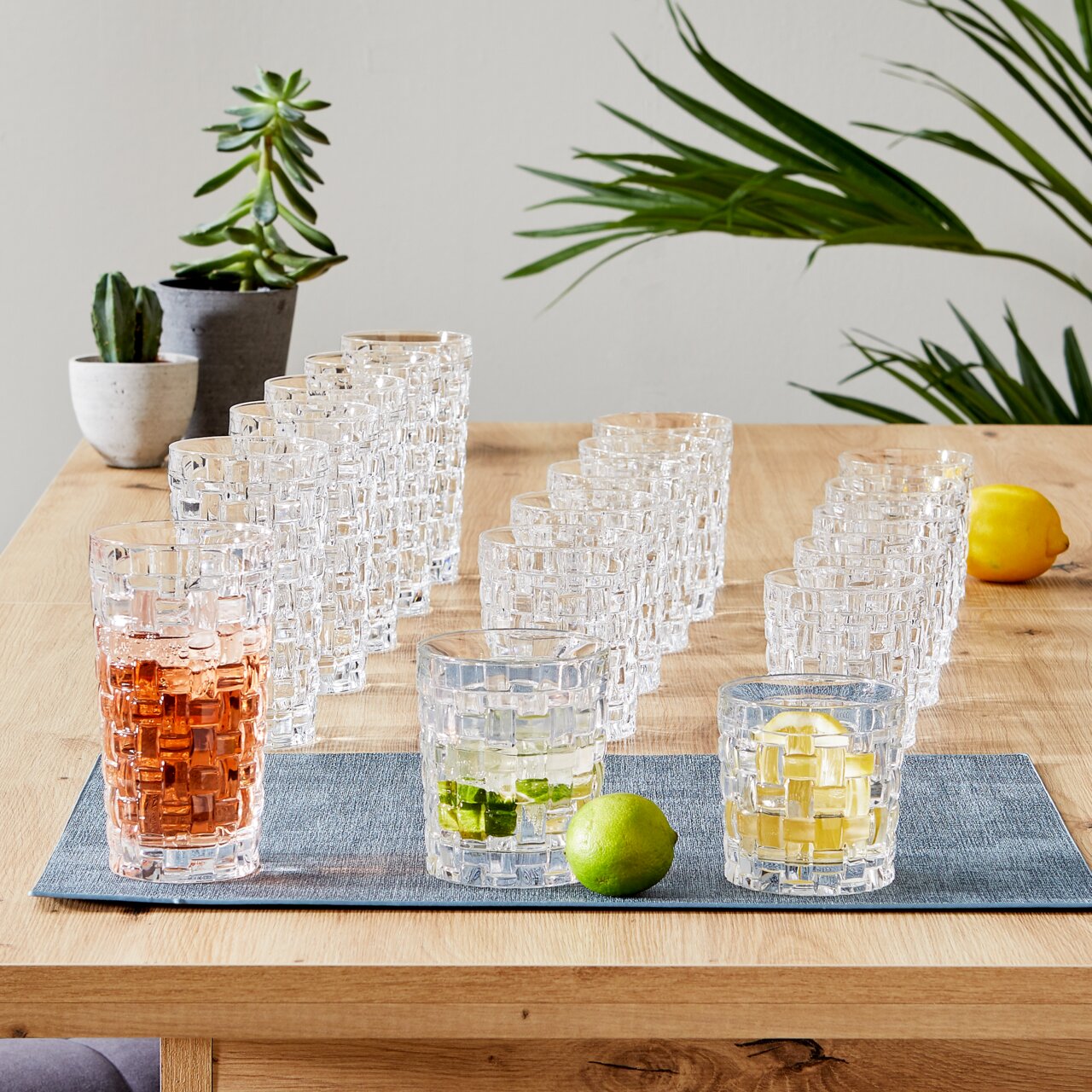 Nachtmann Becherset 18-tlg. BOSSA NOVA Becherset Bossa Nova 18-tlg. auf einem Holztisch, mit Getränken und Limetten, aus seitlicher Perspektive fotografiert.