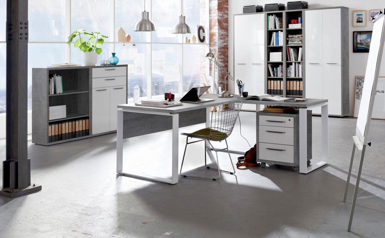 Moderner Eck-Schreibtisch in einem hellen Büro mit großen Fenstern, ausgestattet mit einem Rollcontainer und einem Drahtstuhl, aus der Perspektive von vorne rechts betrachtet.