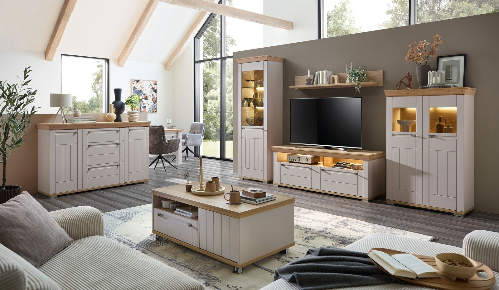 Landscape Vitrine COLMAR Moderne Wohnzimmermöbel in einem hellen Raum mit großen Fenstern, bestehend aus einer Vitrine, einem TV-Schrank und einem Couchtisch, aus hellem Holz und weißen Elementen, seitliche Perspektive.