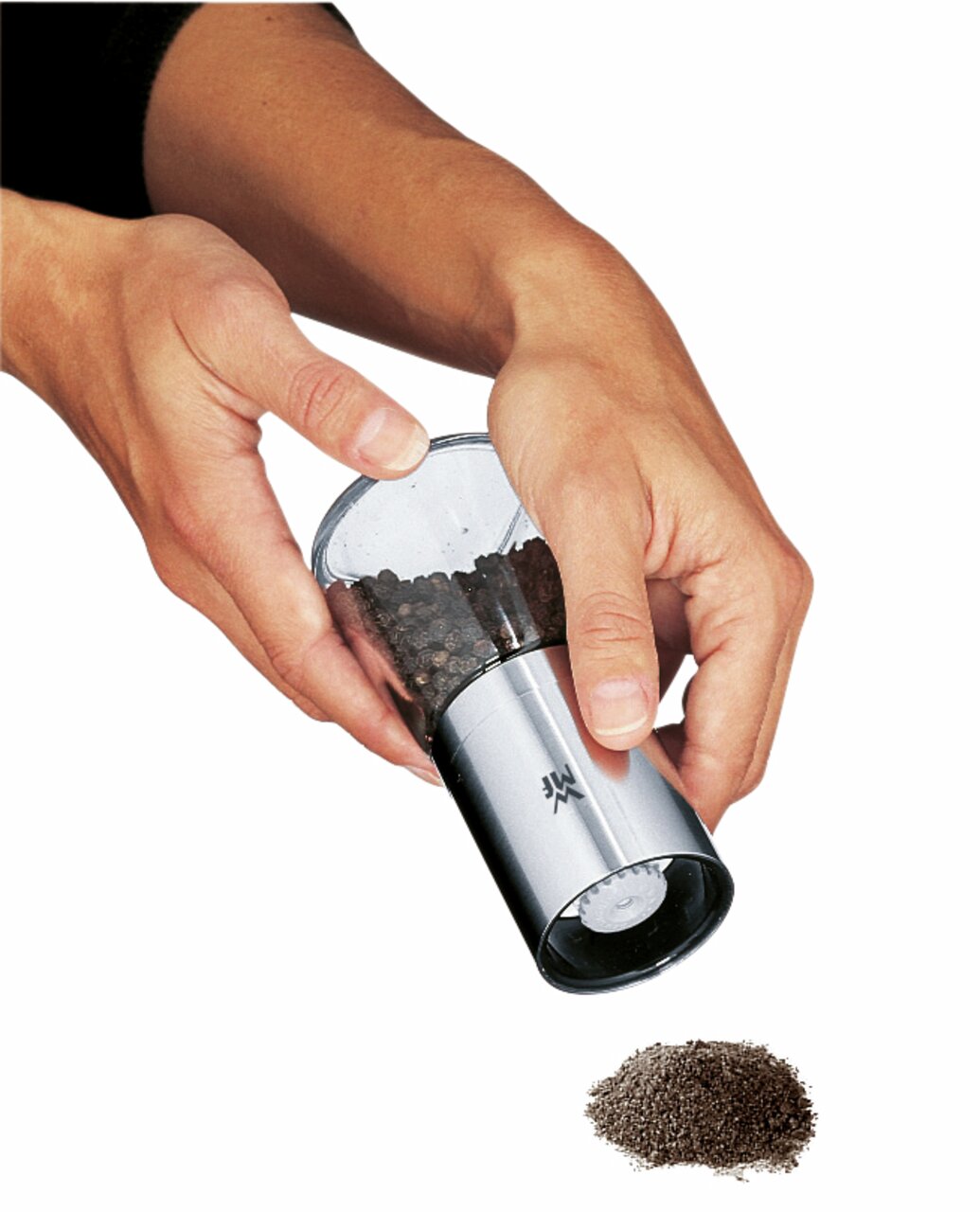 Hände halten eine Gewürzmühle De Luxe aus Edelstahl und Glas, die Pfefferkörner mahlt. Perspektive von oben.