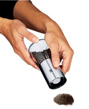 Hände halten eine Gewürzmühle De Luxe aus Edelstahl und Glas, die Pfefferkörner mahlt. Perspektive von oben.