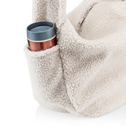 Nahaufnahme einer cremefarbenen Teddy-Fleece-Tasche mit Reißverschluss und Außentasche, in der ein Becher steckt, fotografiert aus seitlicher Perspektive vor weißem Hintergrund.