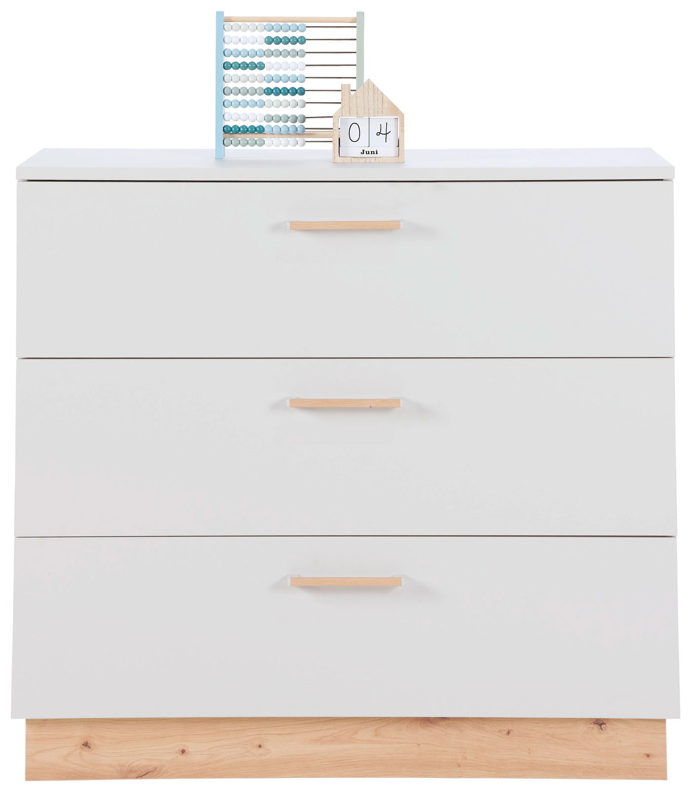 Weiße Wickelkommode mit drei Schubladen und Holzgriffen, frontal fotografiert. Obenauf ein Abakus und ein dekoratives Haus mit Datum.
