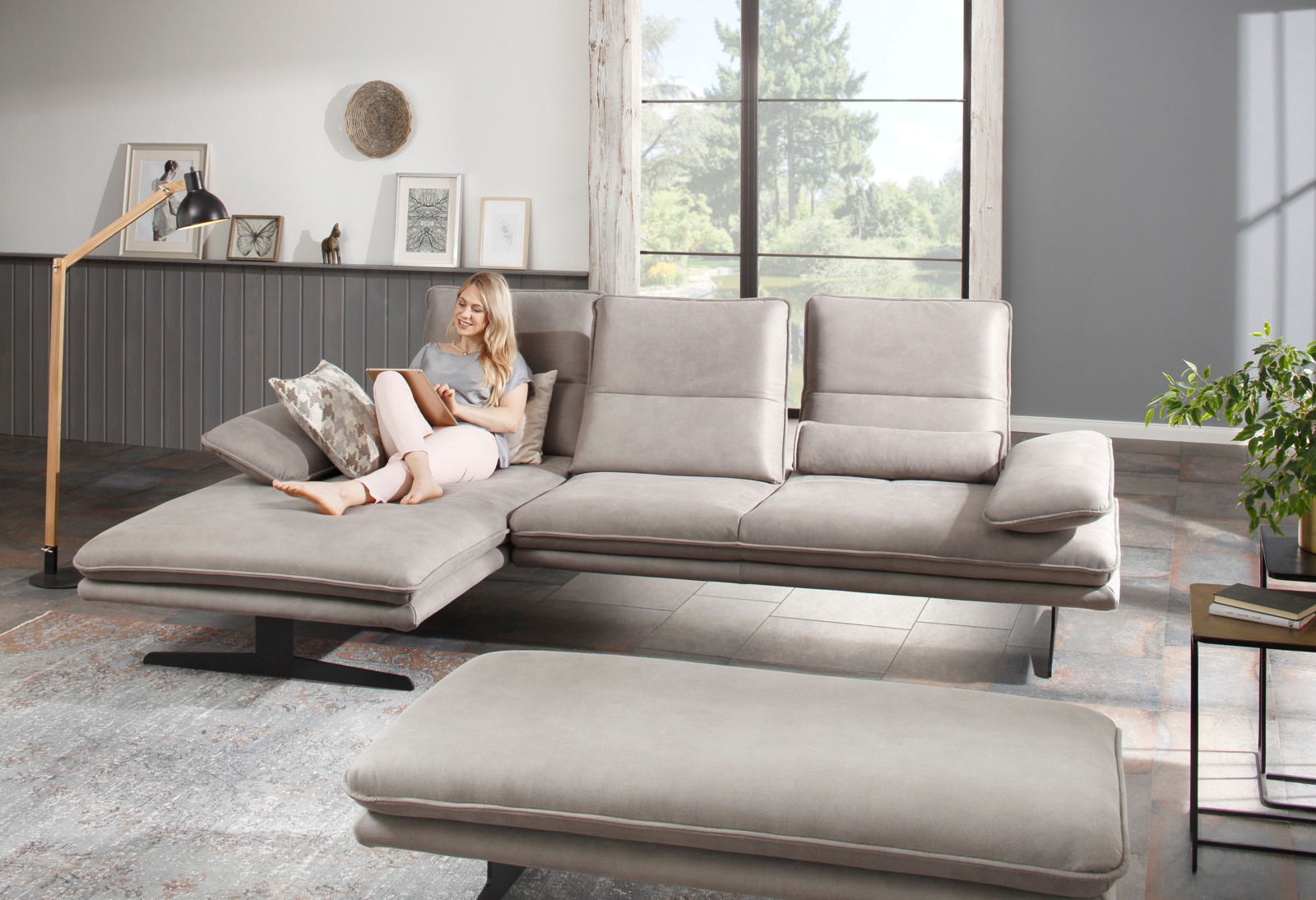 Graue Longchairkombination in einem modernen Wohnzimmer, seitliche Perspektive, mit einer Frau, die auf dem Sofa sitzt und ein Tablet benutzt.