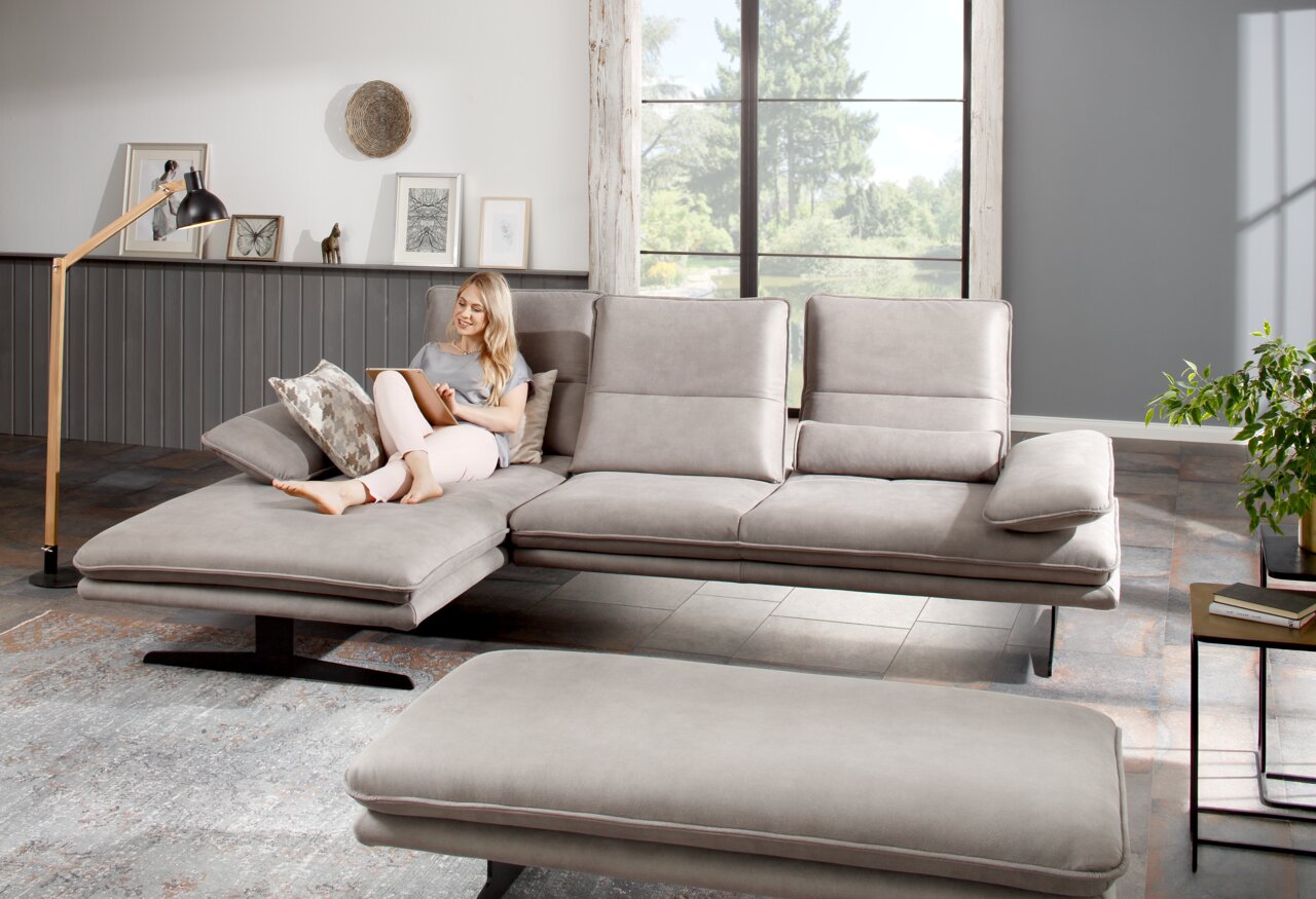 Grijze longchair-set in een moderne woonkamer, gezien vanaf de zijkant, met een vrouw die op de bank zit en een tablet gebruikt.