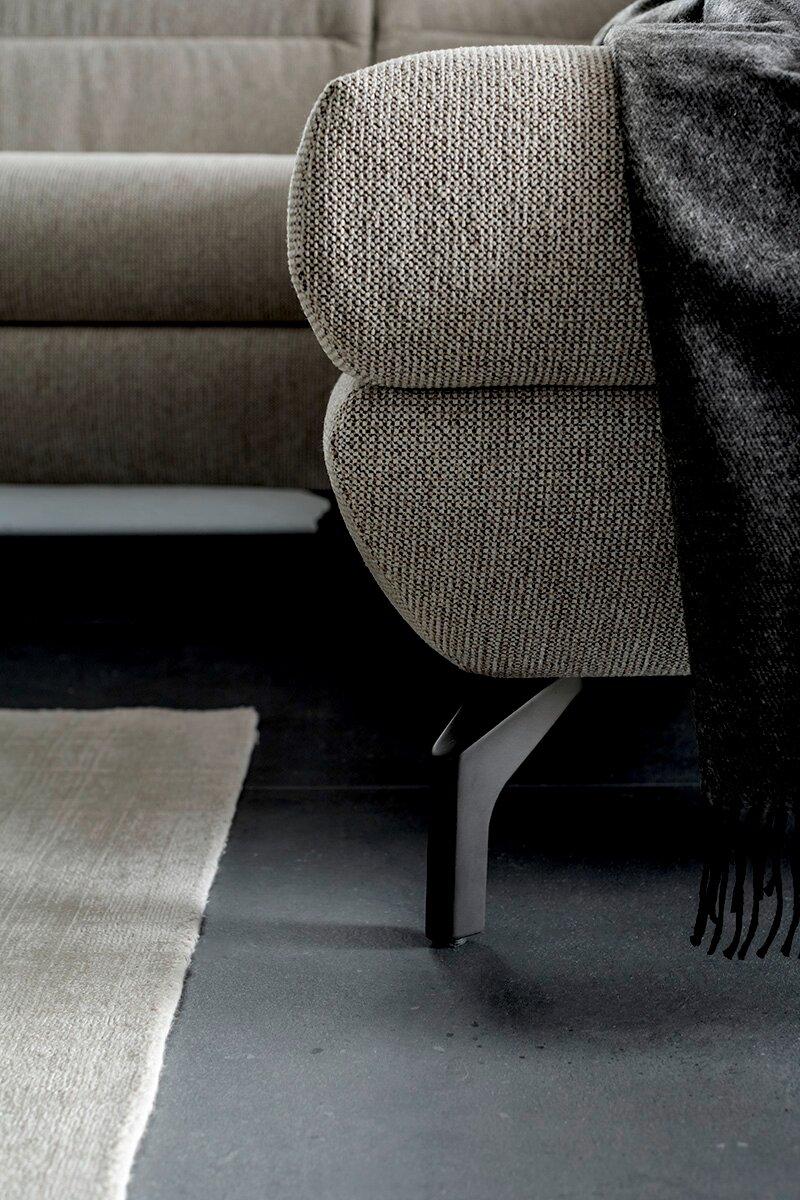 Schöner Wohnen Ecksofa SALERNO Nahaufnahme eines Ecksofas mit grauem Stoffbezug und schwarzem Metallfuß, Perspektive von der Seite.