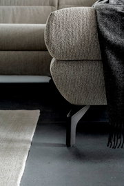 Nahaufnahme eines Ecksofas mit grauem Stoffbezug und schwarzem Metallfuß, Perspektive von der Seite.