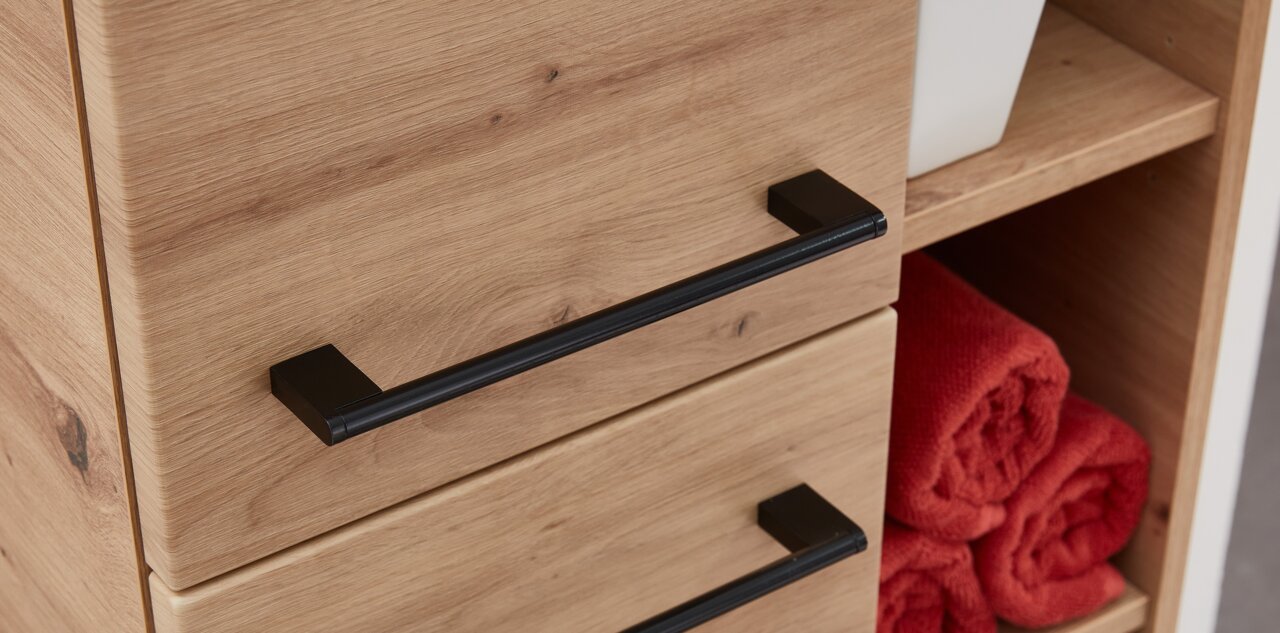 Close-up van een houten midikast met zwarte handgrepen, gezien vanaf de zijkant, met open planken waarop rode handdoeken liggen.