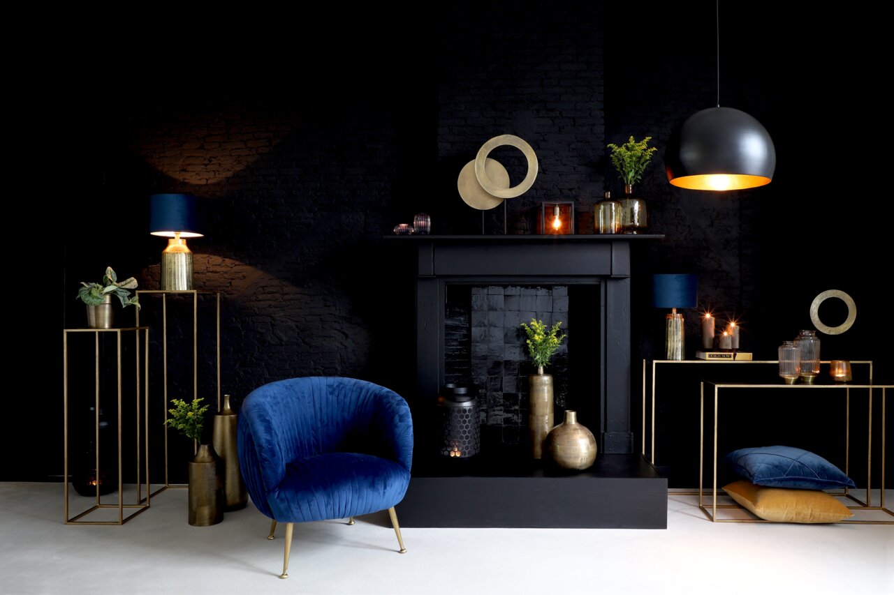 Elegantes Wohnzimmer mit modernem Dekor, darunter ein blaues Samtsofa, goldene Vasen und ein schwarzer Kamin, aus der Frontalperspektive.
