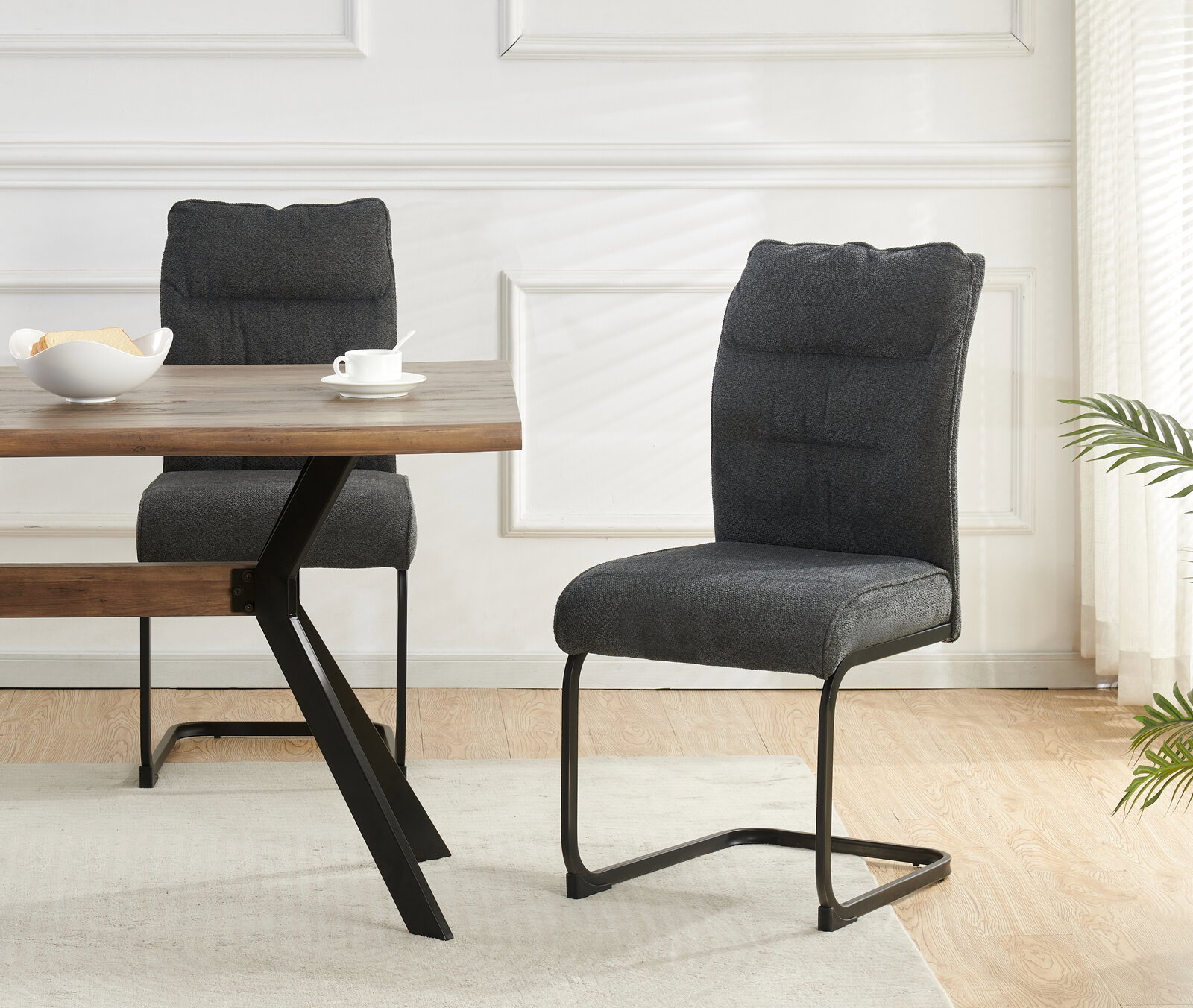 Gepolsterter Esszimmerstuhl in Dunkelgrau mit Steppung und schwarzem Freischwinger-Metallgestell, seitliche Perspektive im Wohn-/Essbereich neben Holztisch