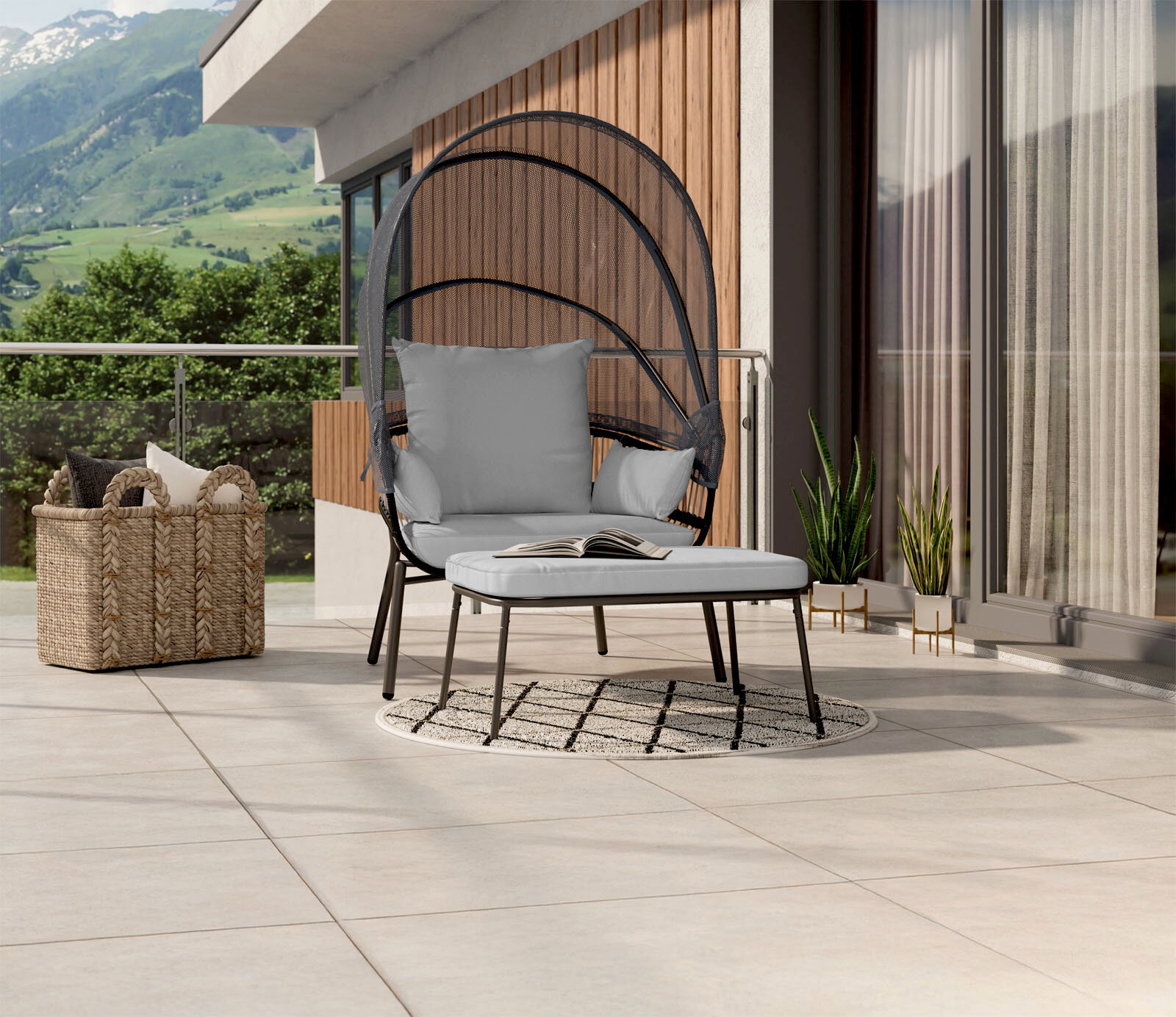 Moderner Loungesessel mit grauen Kissen und passendem Hocker auf einer Terrasse mit Bergblick, seitliche Perspektive.