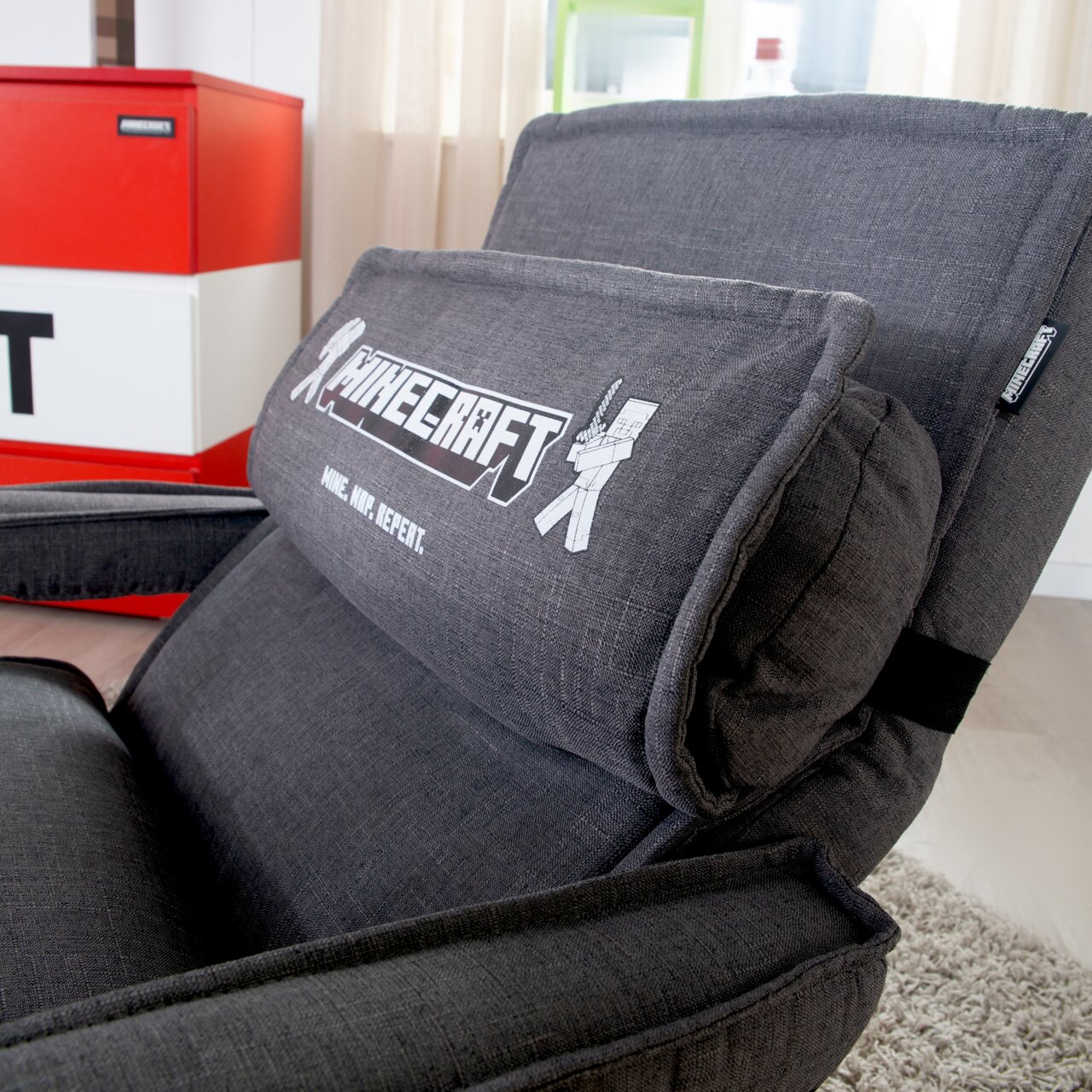 Zwarte, gestoffeerde gamingstoel met Minecraft-logo en de tekst „Mine. Nurf. Repeat.“ op het rugkussen, gefotografeerd vanuit een schuin vooraanzicht in de woonkamer.