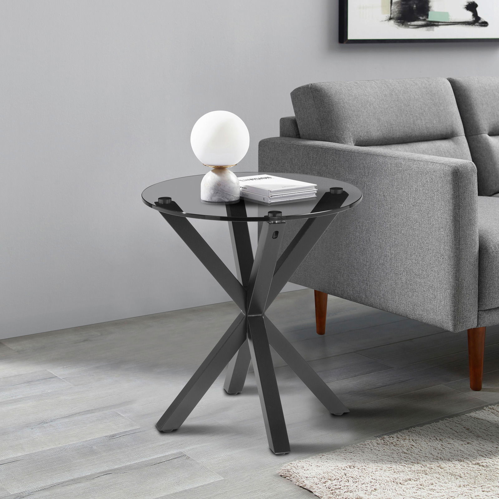 XORA Beistelltisch NICO Moderner Beistelltisch mit schwarzer Glasplatte und gekreuztem Metallgestell, seitliche Perspektive neben einem grauen Sofa.