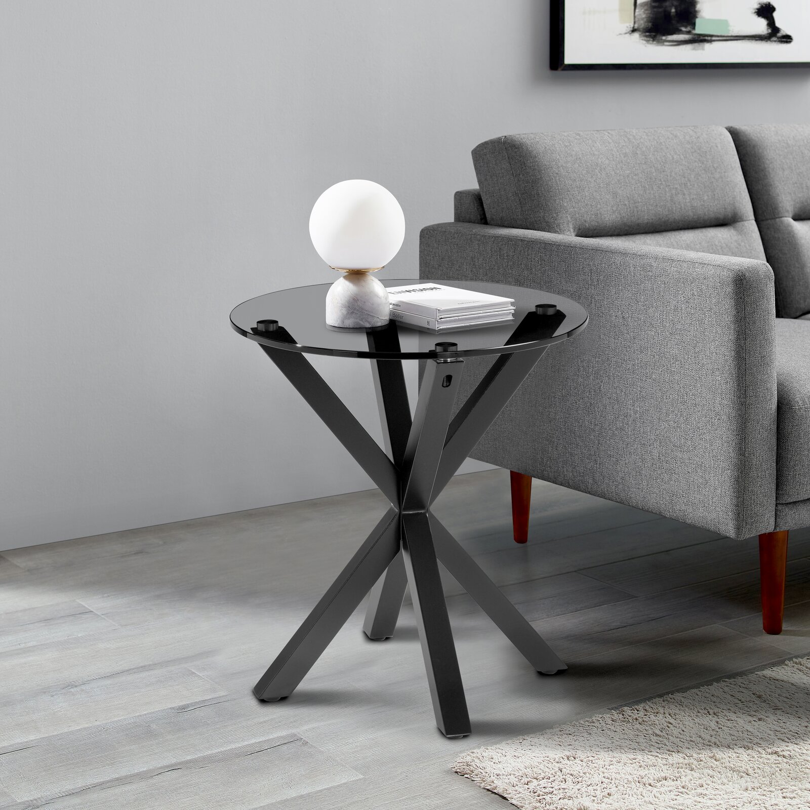 XORA Beistelltisch NICO Moderner Beistelltisch mit schwarzer Glasplatte und gekreuztem Metallgestell, seitliche Perspektive neben einem grauen Sofa.