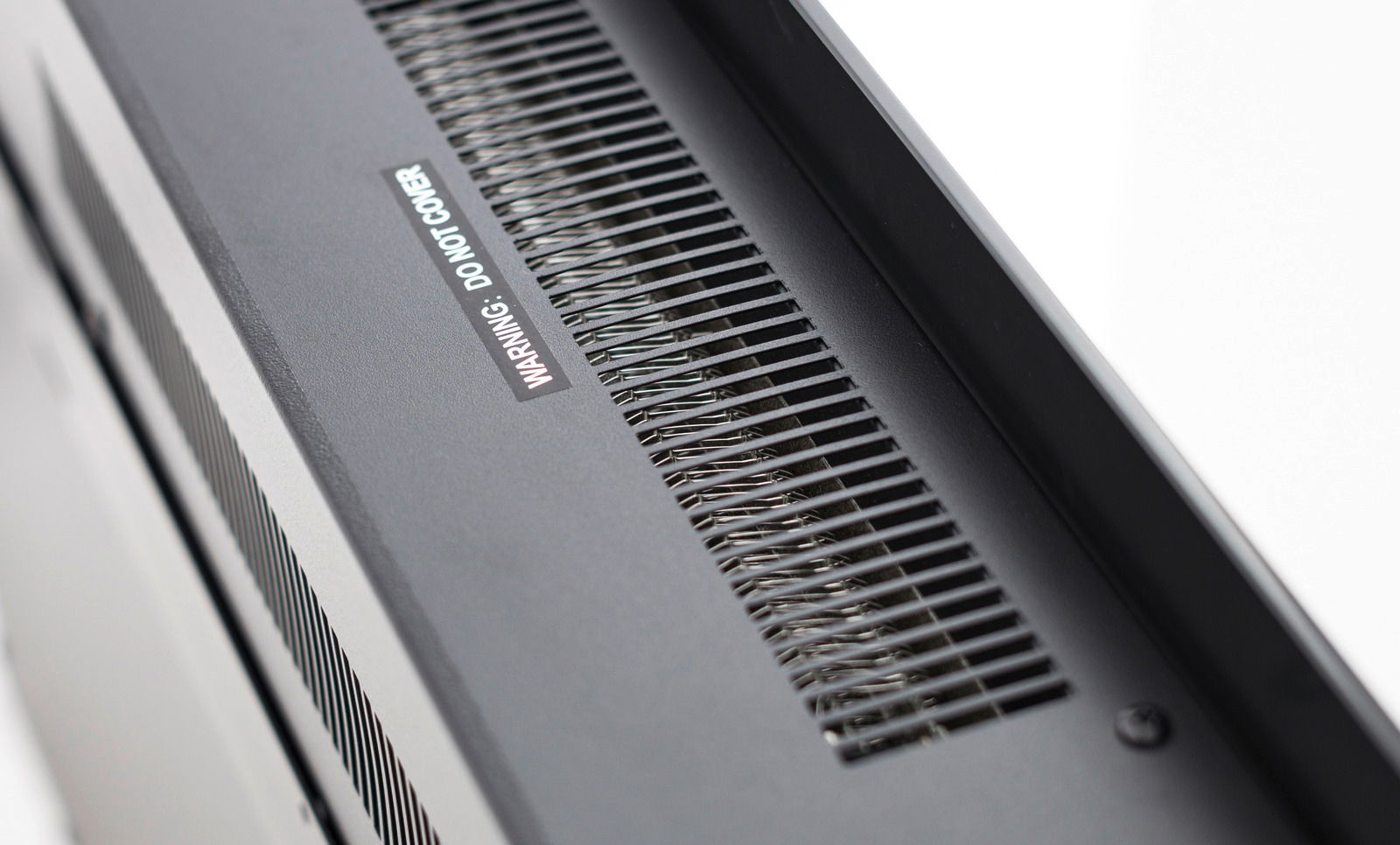 Nahaufnahme der Oberseite eines Elektrokamins mit Lüftungsgitter und Warnhinweis, Perspektive von schräg oben.