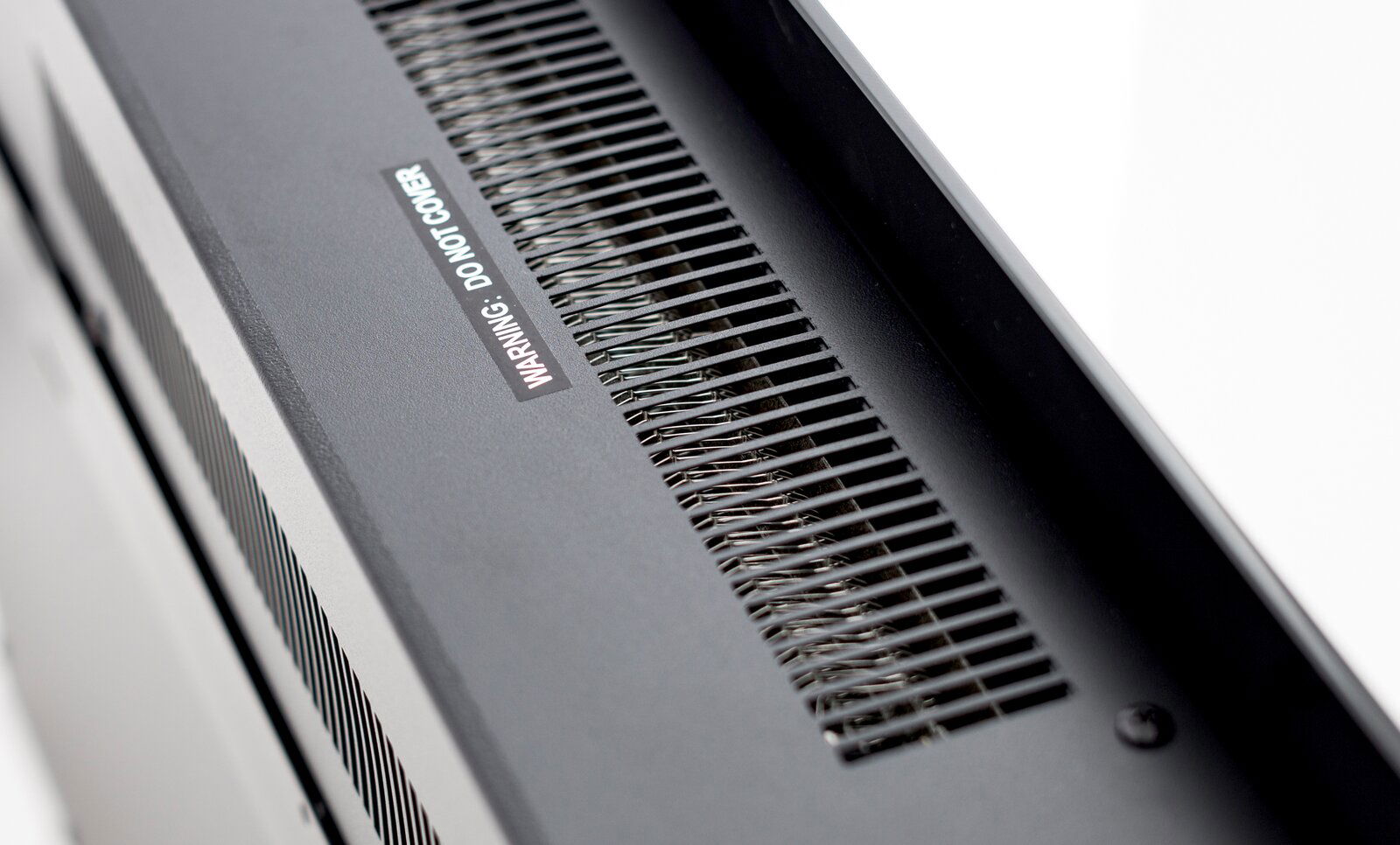 Nahaufnahme der Oberseite eines Elektrokamins mit Lüftungsgitter und Warnhinweis, Perspektive von schräg oben.