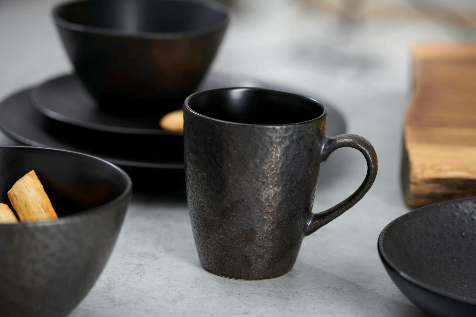 Nahaufnahme eines stilvollen, dunklen Frühstücksservices mit Tasse, Schalen und Tellern auf einem Tisch.