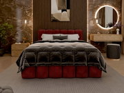 Luxuriöses Polsterbett in einem stilvollen Schlafzimmer, frontal aufgenommen. Das Bett hat ein rotes, gepolstertes Kopfteil und ist mit einer dunklen, gesteppten Decke bedeckt. Die Umgebung ist modern mit einem runden, beleuchteten Spiegel und eleganten M