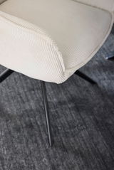 Nahaufnahme eines cremefarbenen Armlehnstuhls mit geripptem Stoffbezug und schwarzen Metallbeinen, von oben betrachtet.