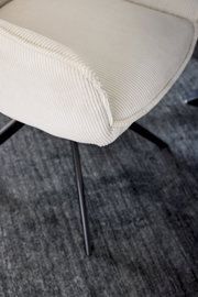 Nahaufnahme eines cremefarbenen Armlehnstuhls mit geripptem Stoffbezug und schwarzen Metallbeinen, von oben betrachtet.