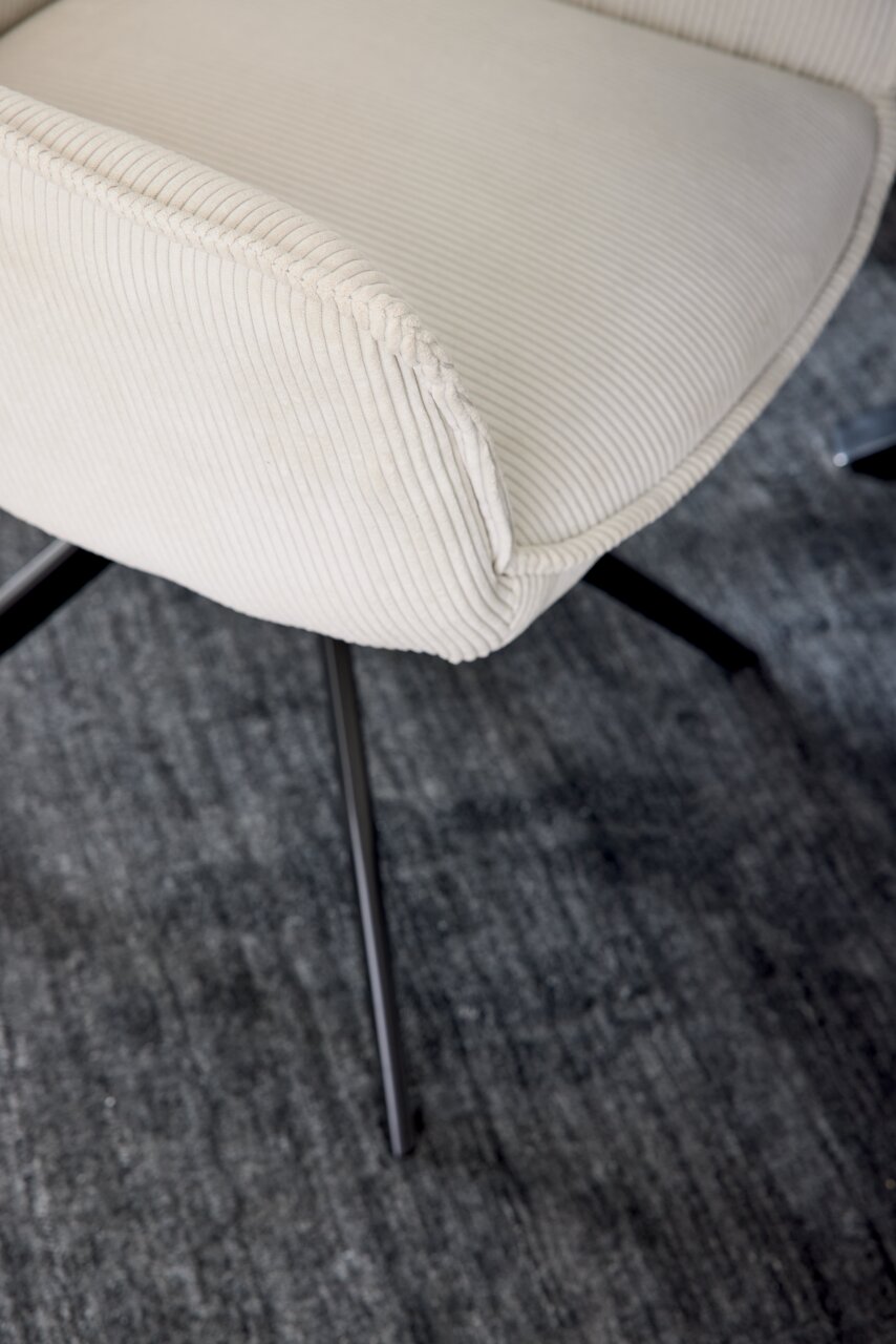 Nahaufnahme eines cremefarbenen Armlehnstuhls mit geripptem Stoffbezug und schwarzen Metallbeinen, von oben betrachtet.