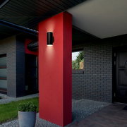 Moderne schwarze Akku-Außenwandleuchte an einer roten Wand, seitliche Perspektive