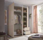 Offener, moderner Kleiderschrank in Beige mit Kleiderstange, Regalfächern und zwei ausgezogenen Schubladen, fotografiert aus leicht schräger Frontperspektive im hellen Schlafzimmer neben großem Fenster mit rosa Vorhang.