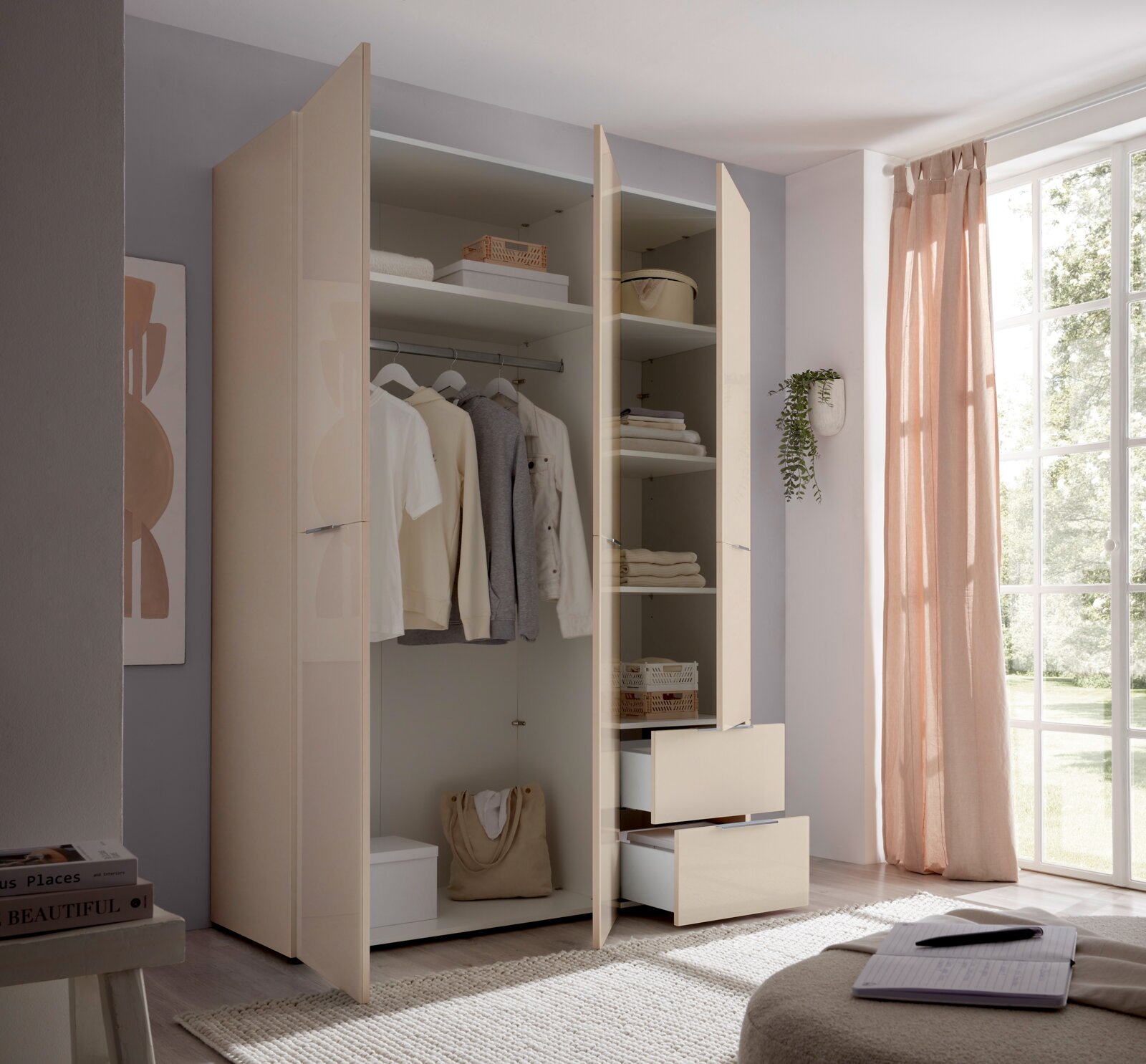 Offener, moderner Kleiderschrank in Beige mit Kleiderstange, Regalfächern und zwei ausgezogenen Schubladen, fotografiert aus leicht schräger Frontperspektive im hellen Schlafzimmer neben großem Fenster mit rosa Vorhang.