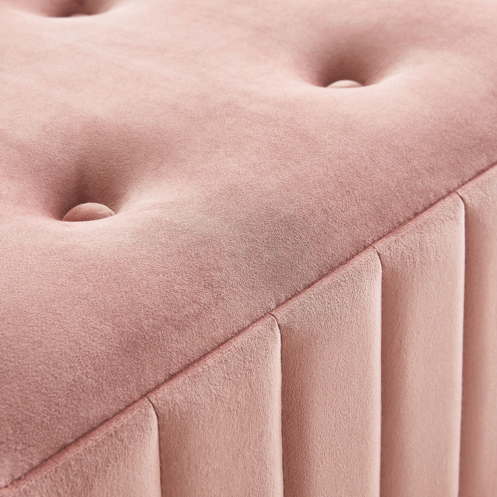 Nahaufnahme einer rosa gepolsterten Hockerbank mit Knopfdetails und vertikalen Nähten, perspektivisch von oben fotografiert.