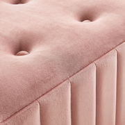 Nahaufnahme einer rosa gepolsterten Hockerbank mit Knopfdetails und vertikalen Nähten, perspektivisch von oben fotografiert.