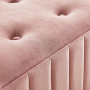 Nahaufnahme einer rosa gepolsterten Hockerbank mit Knopfdetails und vertikalen Nähten, perspektivisch von oben fotografiert.