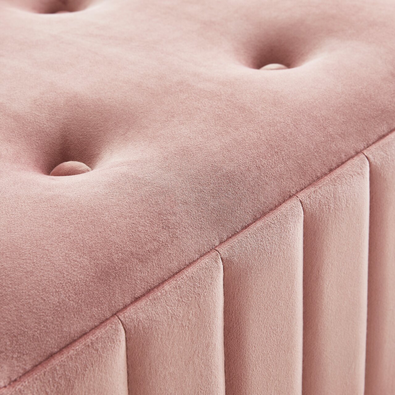 Nahaufnahme einer rosa gepolsterten Hockerbank mit Knopfdetails und vertikalen Nähten, perspektivisch von oben fotografiert.