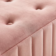 Nahaufnahme einer rosa gepolsterten Hockerbank mit Knopfdetails und vertikalen Nähten, perspektivisch von oben fotografiert.